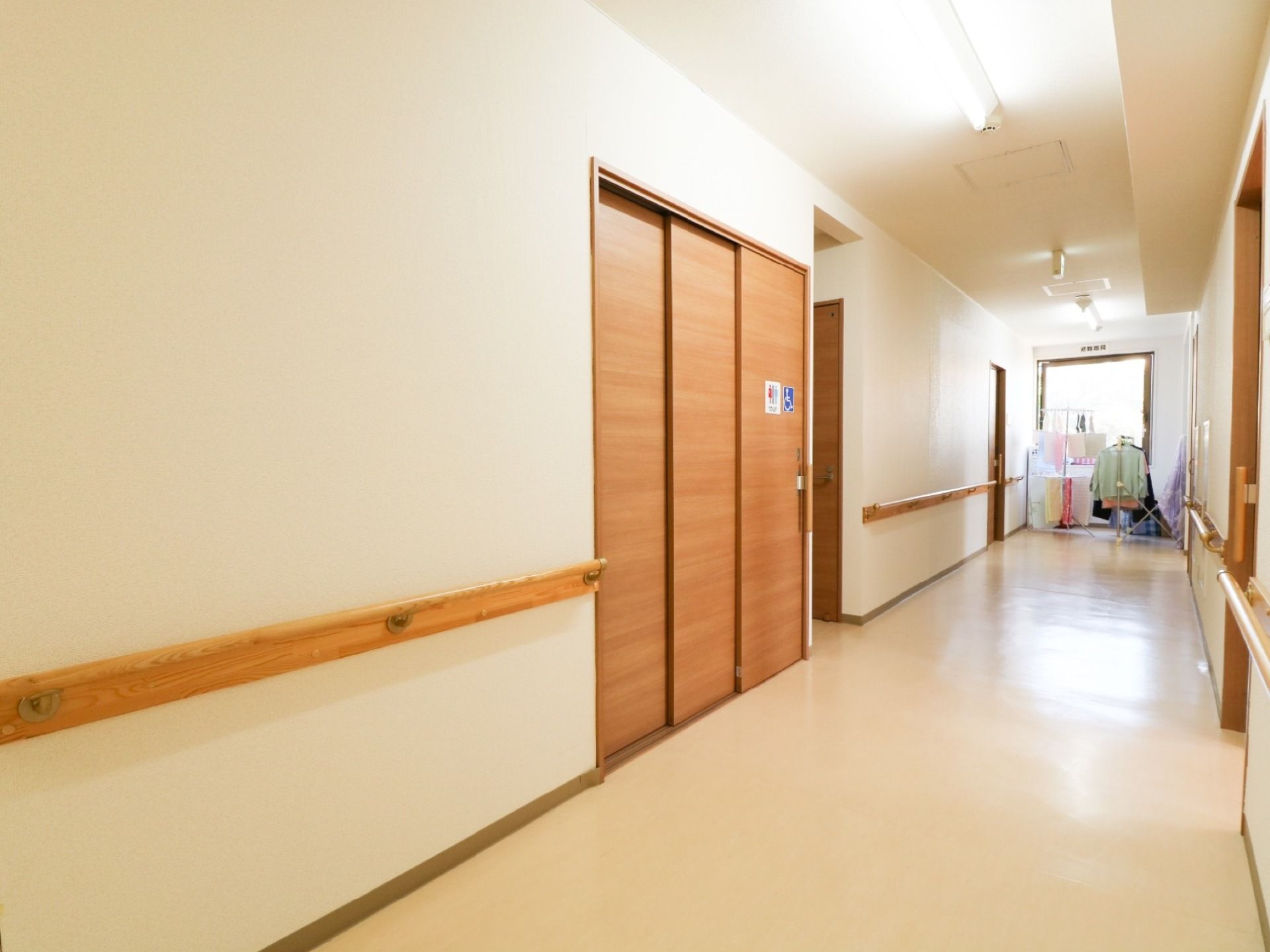 通路の突き当たりに洗濯物が干してある。左側に木製の大きなドアが設置されており、トイレと車椅子の表示が貼られている。