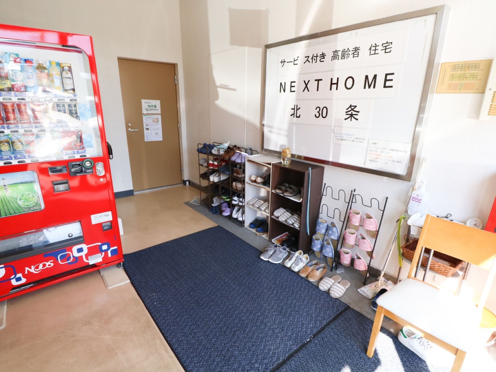 玄関には滑り止めマットが敷かれ、シューズラックや自動販売機が設置されている。壁面に取り付けてあるホワイトボードに施設名称が表示されている。
