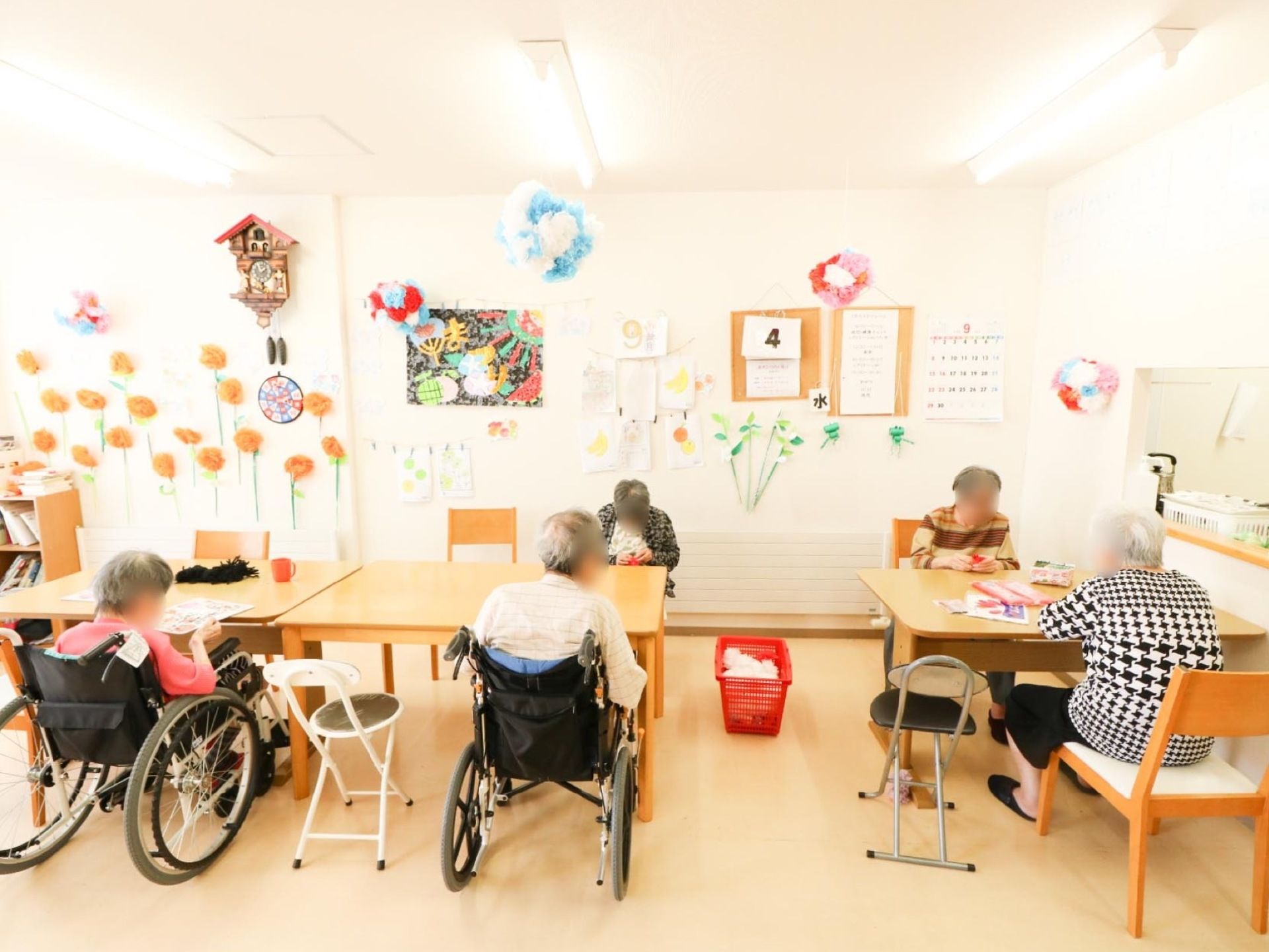 制作物が展示され、壁面装飾が施されている広間である。数名の入居者様がテーブルに向かいながら作業をしている。