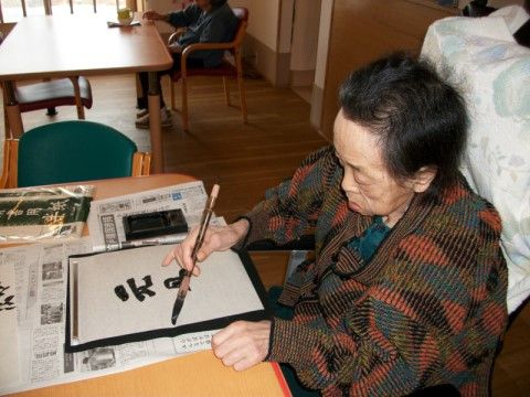 デスクに新聞を敷いて書道をされている女性の入居者様