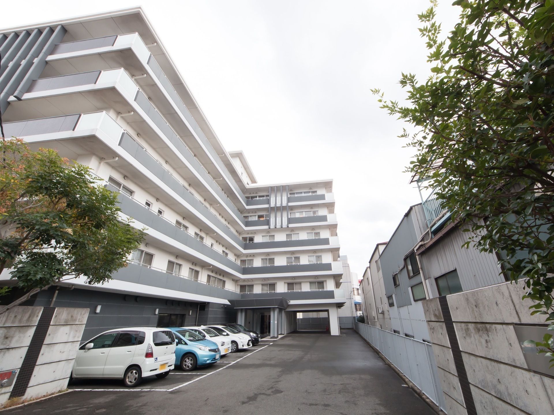 清潔感のある白とグレーの外壁の７階建てのマンション風のホーム。玄関前にはアスファルトで舗装された駐車場がある。