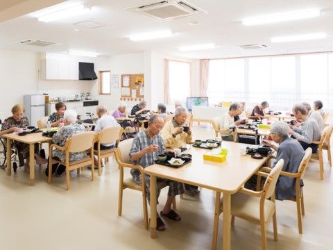 明るい木目調のテーブルセットの席で、食事をされる入居者様皆さま