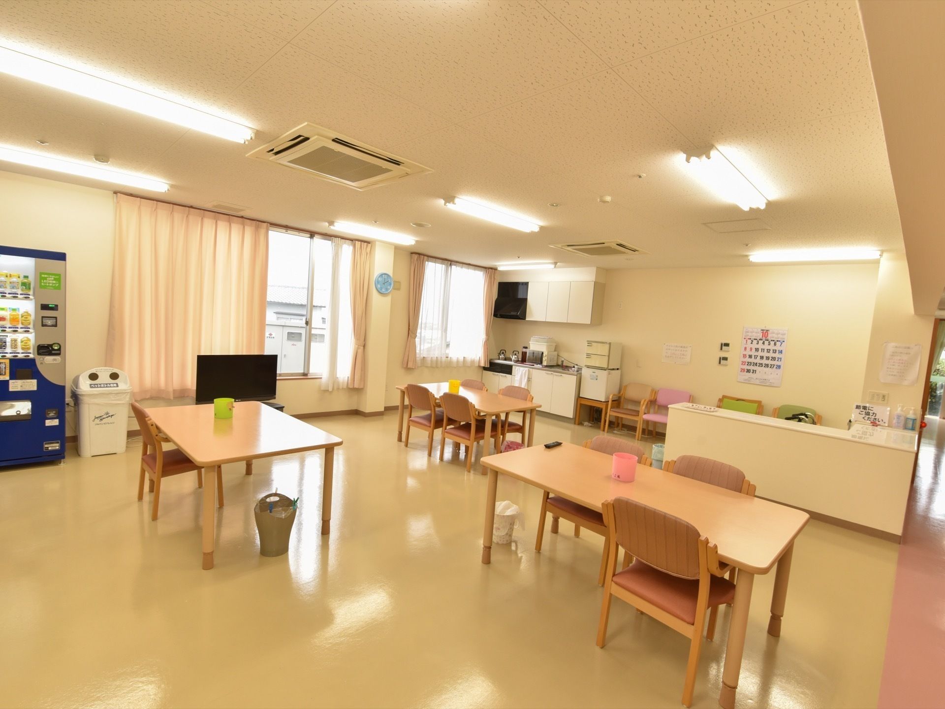 食堂には茶色いテーブルと椅子が並べられている。各テーブルの上にはカラフルな容器、下には小さなゴミ箱が置かれている。