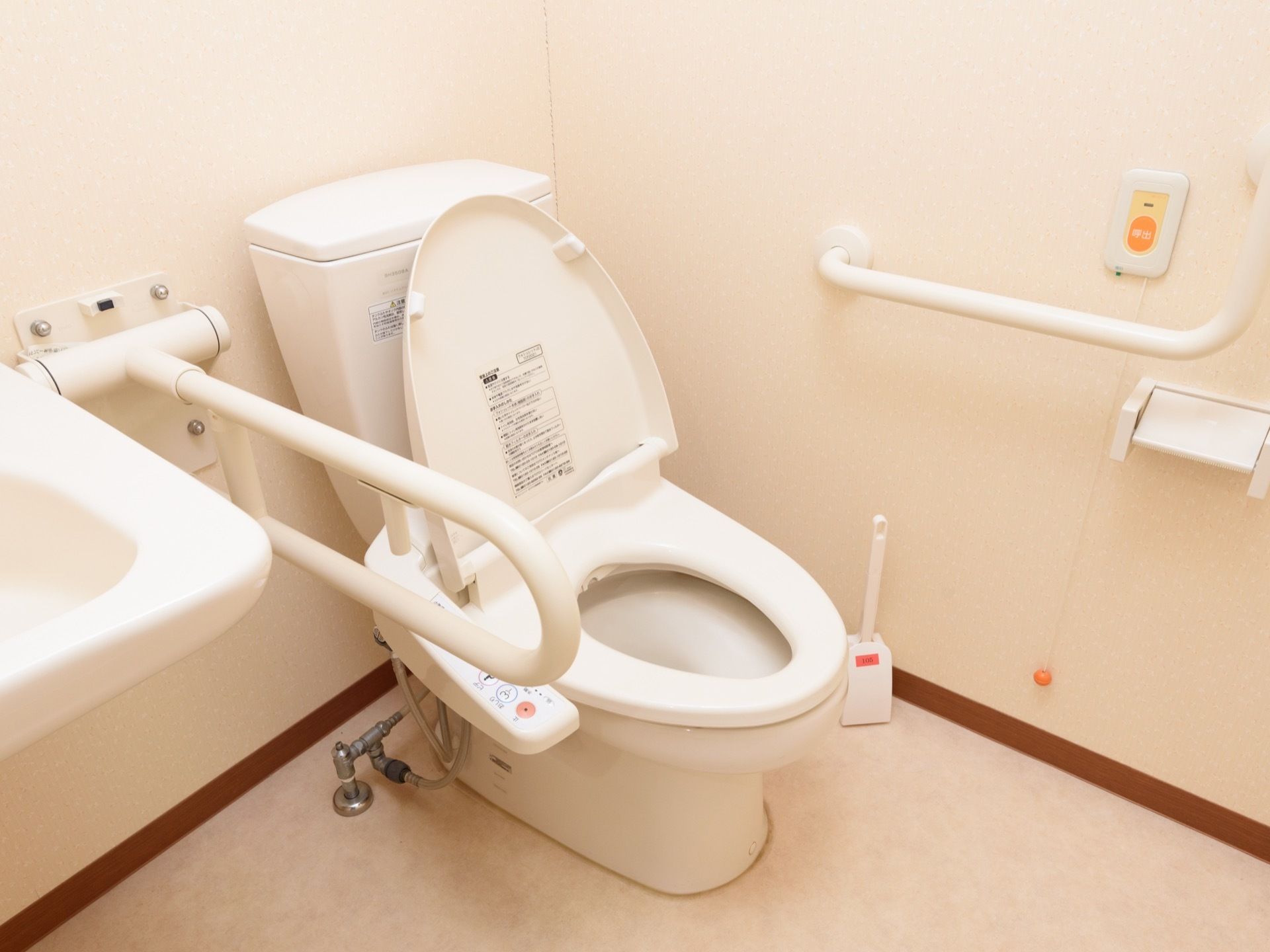 便器の脇に、がっちりとした手すりと洗面台が並んでいる。壁にも手すりがあり、緊急呼び出しブザーが備わっている。