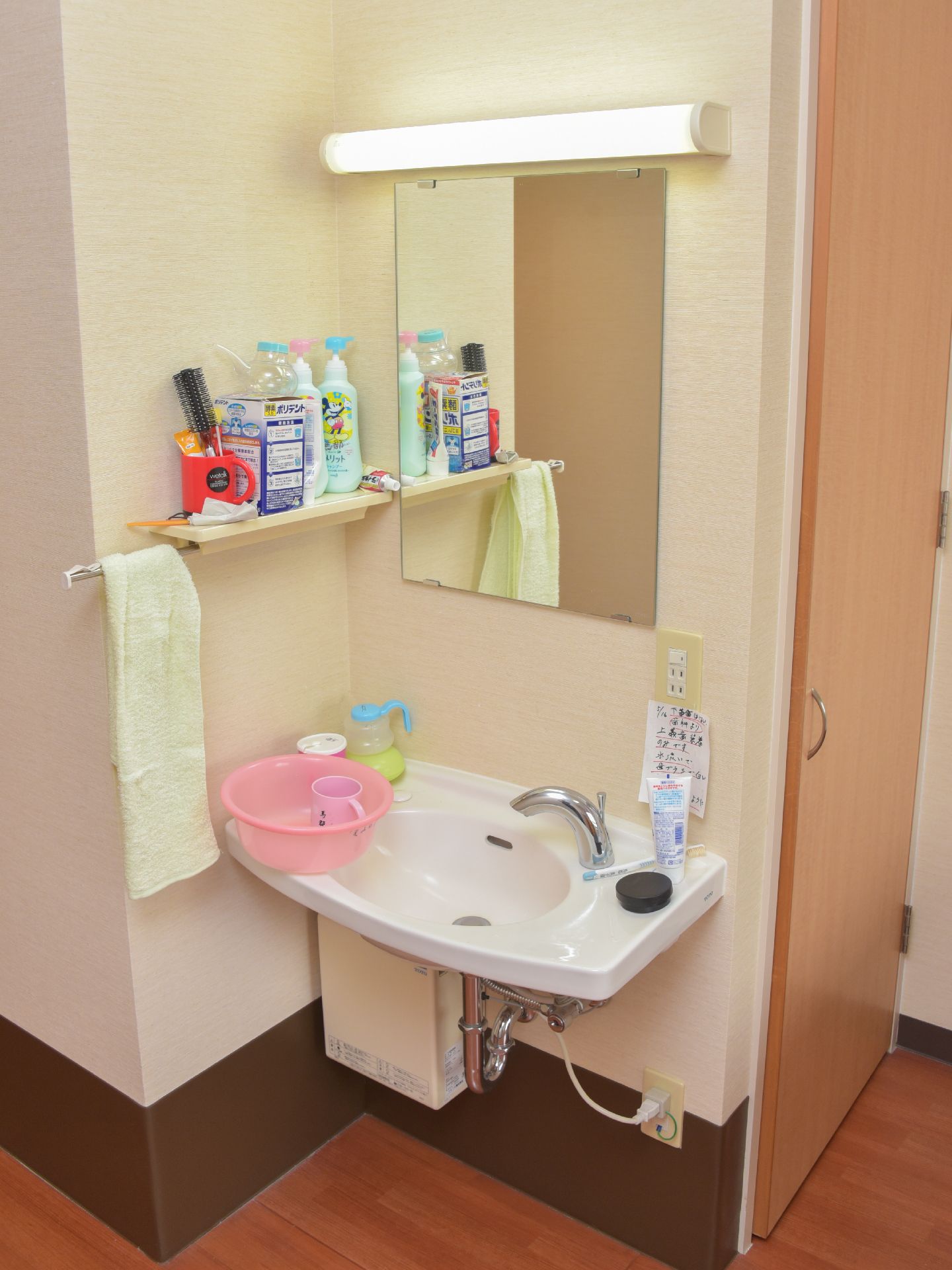 個室についている車いすでも使用しやすい足元が無いタイプのコンパクトな洗面台。鏡やタオル掛け、照明がついている。