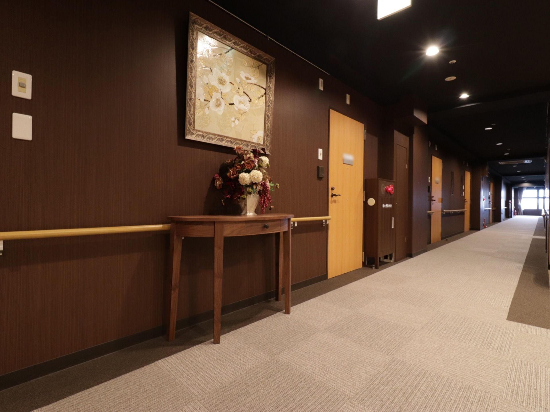 廊下の壁沿いに飾り台に花が装飾されている。大きな絵画も掛けられている。廊下沿いには、手すりが設けられている。