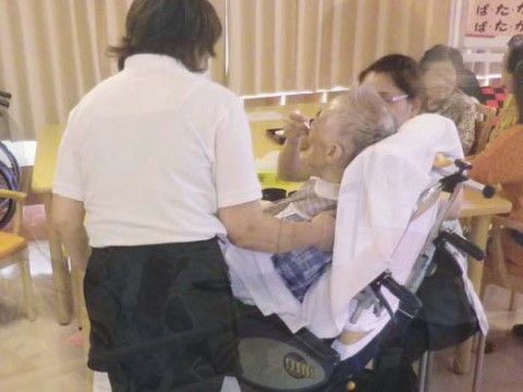 車椅子をご利用の男性に食事のサポートをしている２名の女性スタッフ