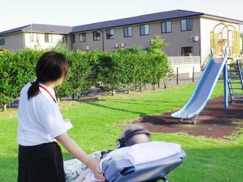 芝生のある公園で施設を眺めている、簡易ベッドに横たわる入居者様