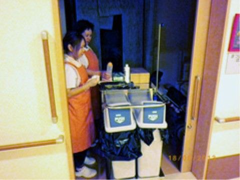 居室内を清掃中のオレンジエプロン姿の２名の女性スタッフ