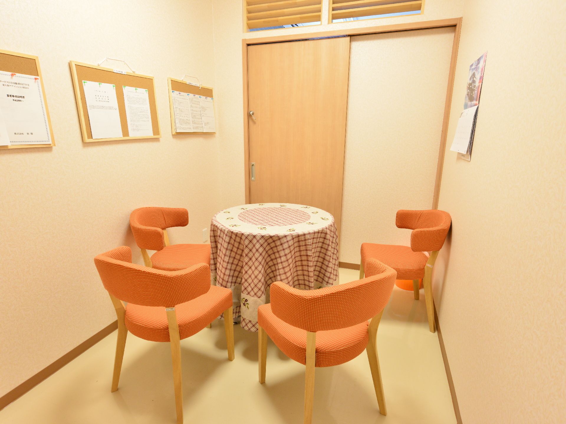 ベージュ系のシンプルな内装で、4脚のオレンジ色の椅子が丸いテープを囲んでいる。プライバシーが保たれている。