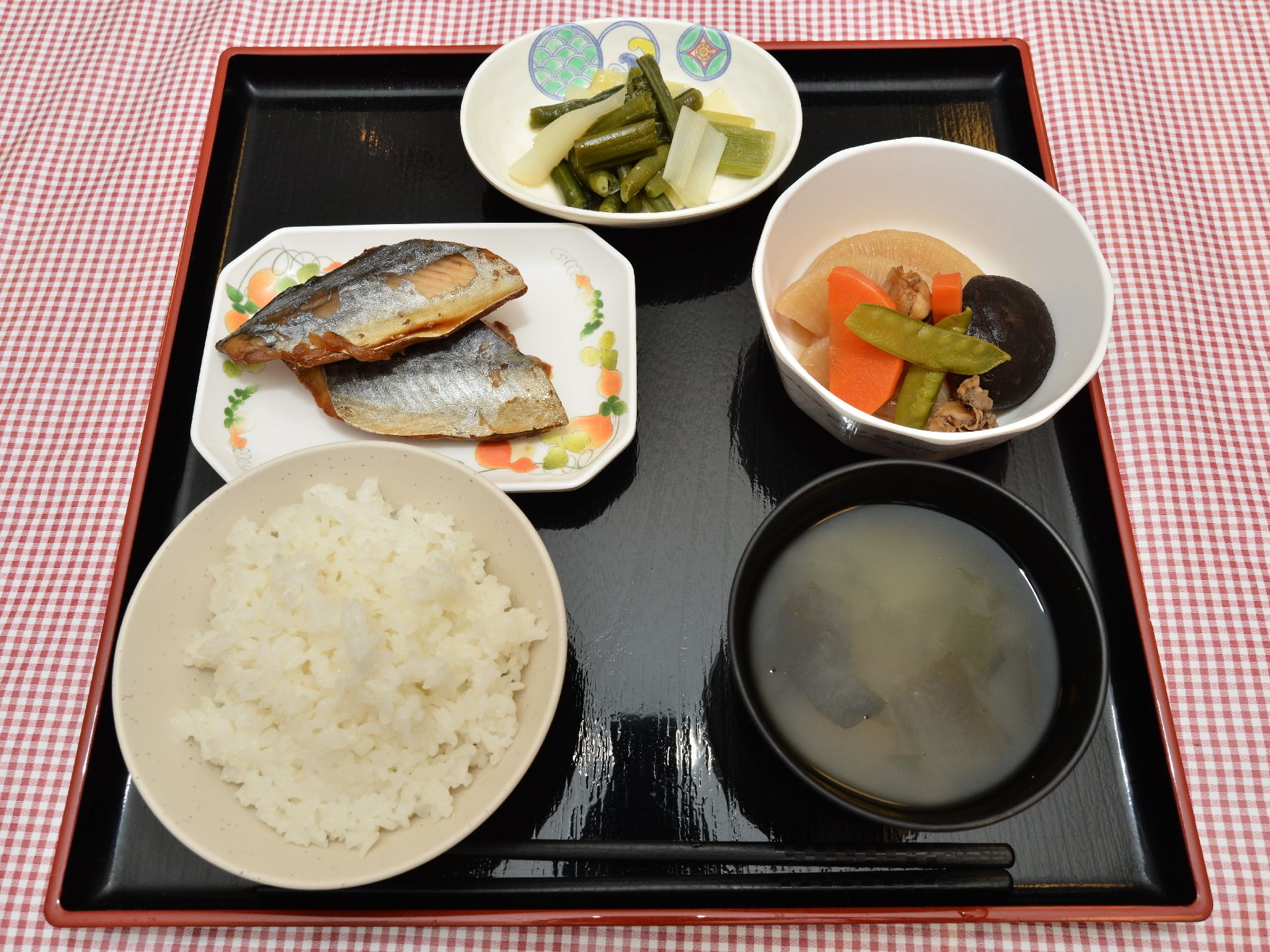 ご飯、味噌汁、主菜と副菜が2品ついた食事。黒のお盆が使われ、食器の白さや食べ物の色が鮮やかに見える。