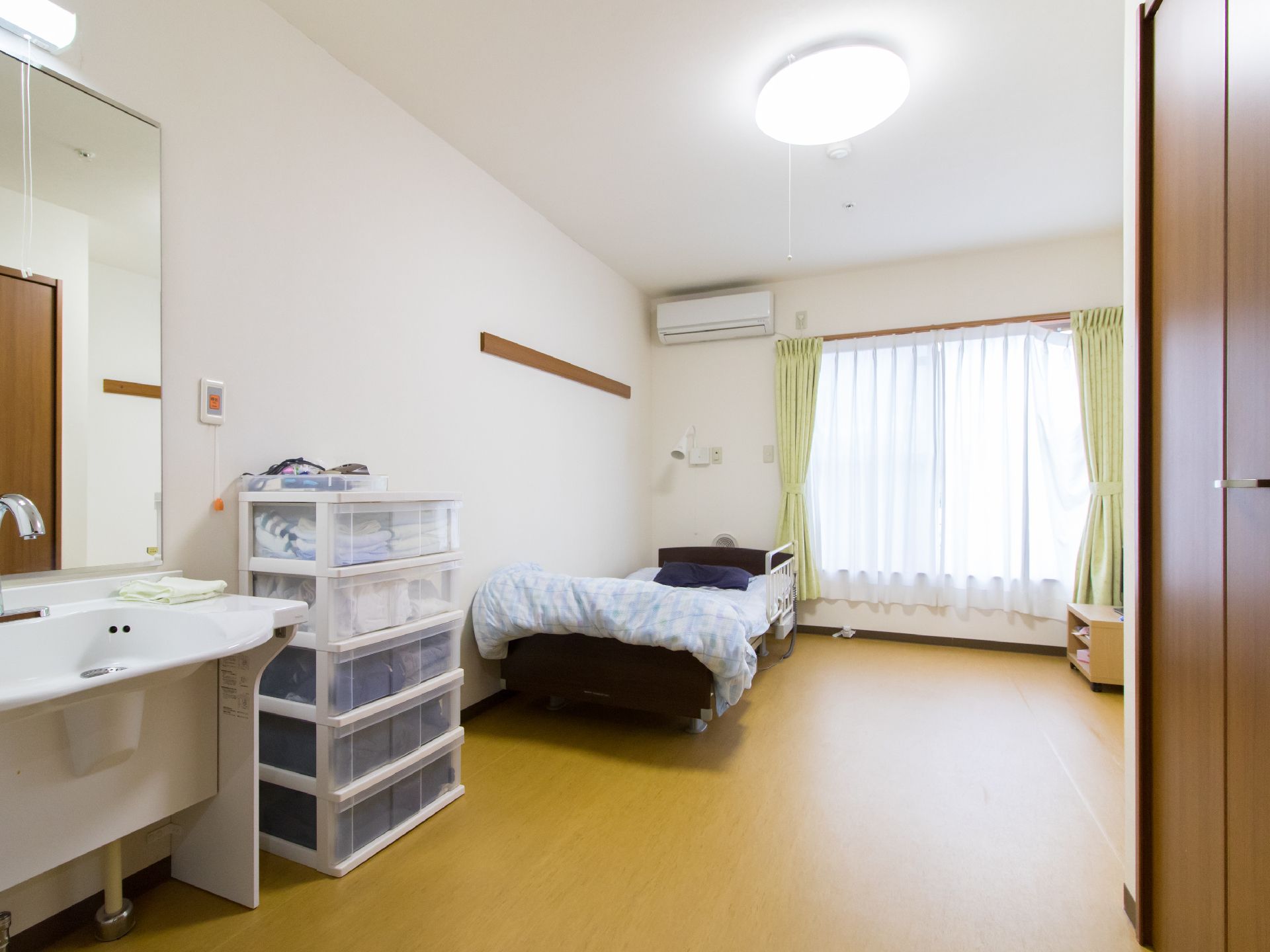カーテンが掛かった窓がある部屋にはベッドが置かれている。また透明の衣装ケースも5段に積み重ねられている。