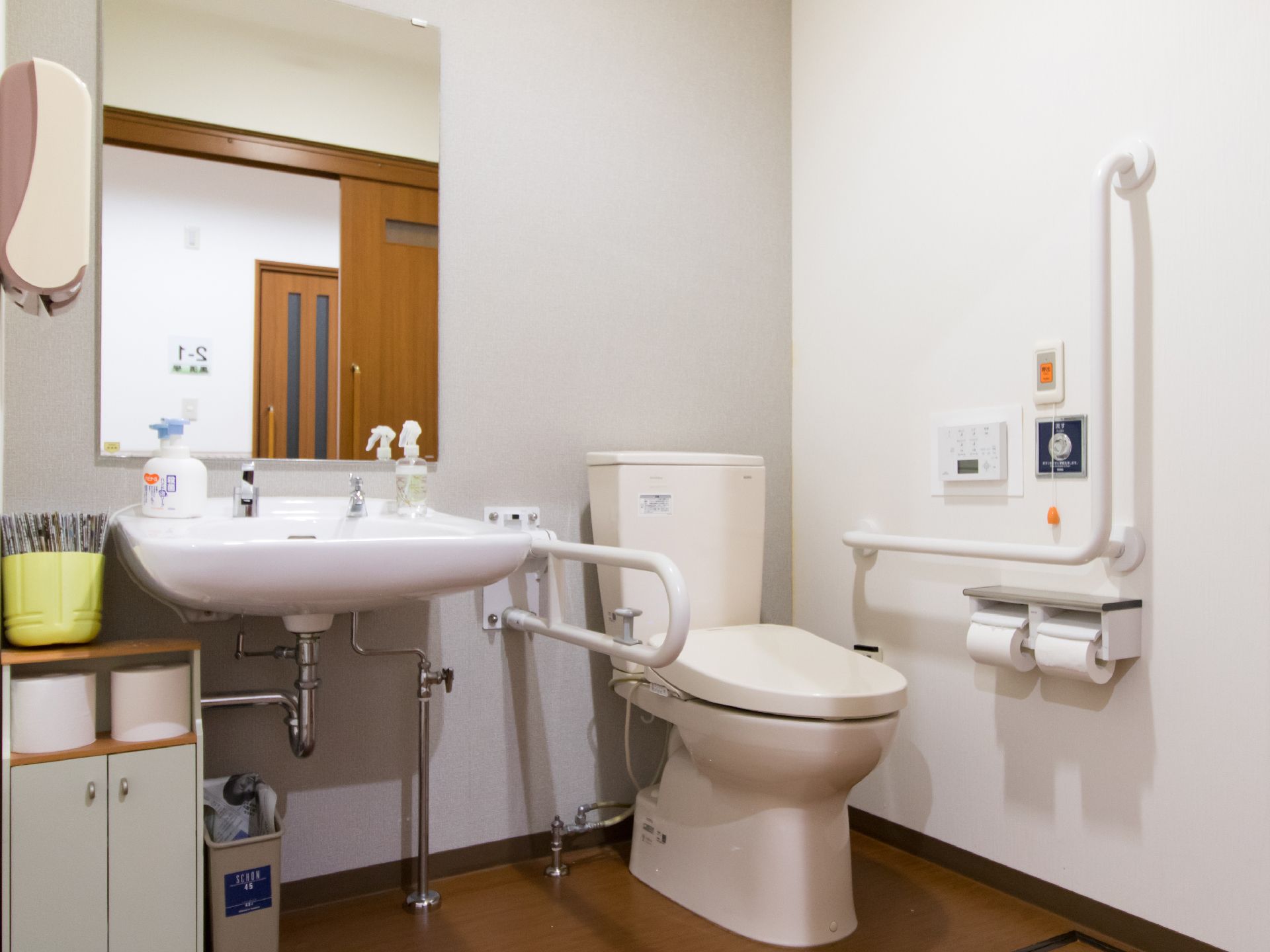 トイレと洗面台が並んだスペースがある。トイレの壁側にはL字型の手すりが付いていて、呼び出しボタンもある。