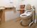 ストライプの壁紙のトイレで、両サイドに手すりがあるので、つかまりながら立ち居ができる。茶色の収納棚がある。手を洗う洗面台が設けてある。