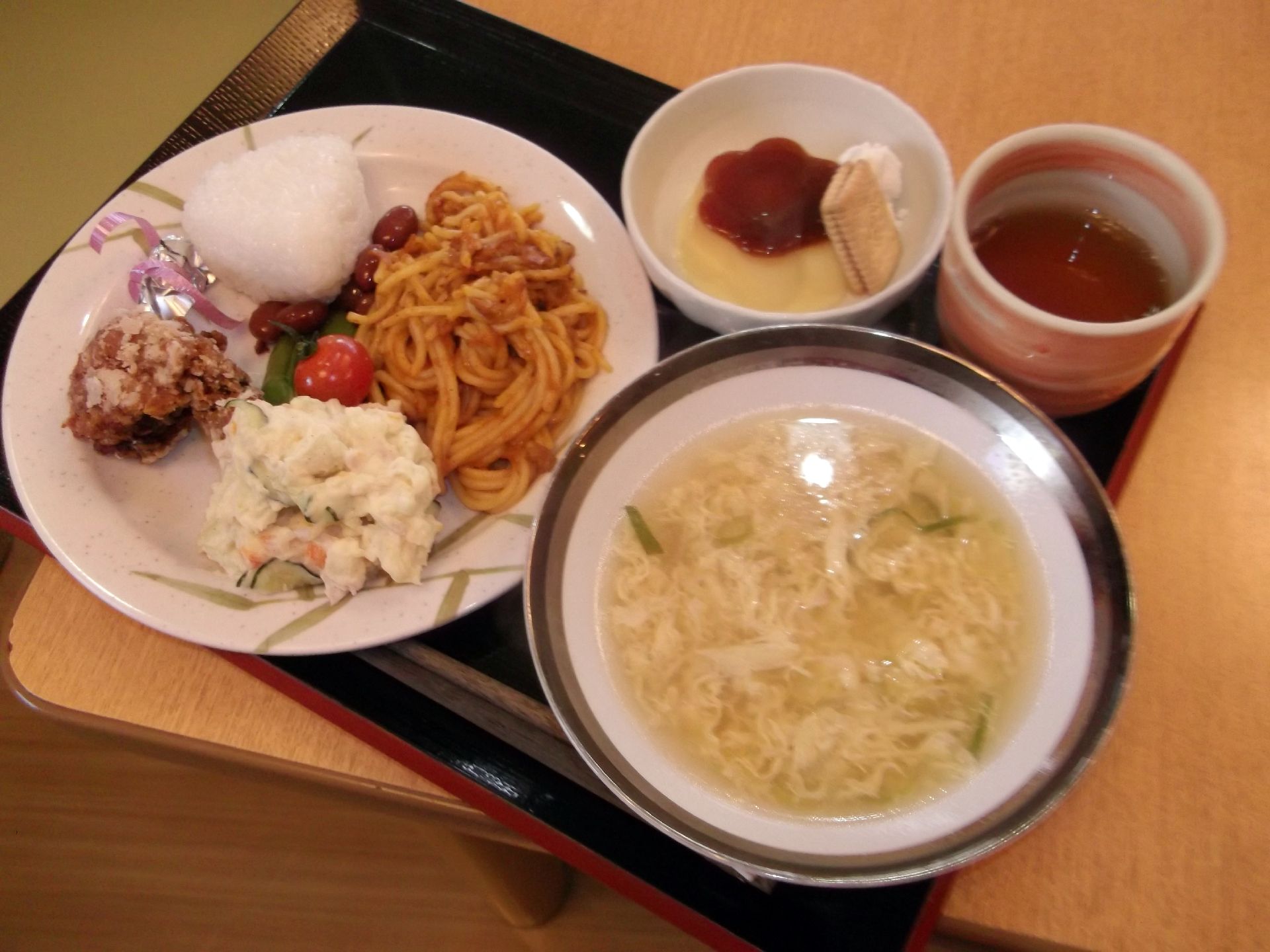 ワンプレートにおにぎり、パスタ料理、ポテトサラダがのったものと、卵の中華風スープがお盆に置いてある。