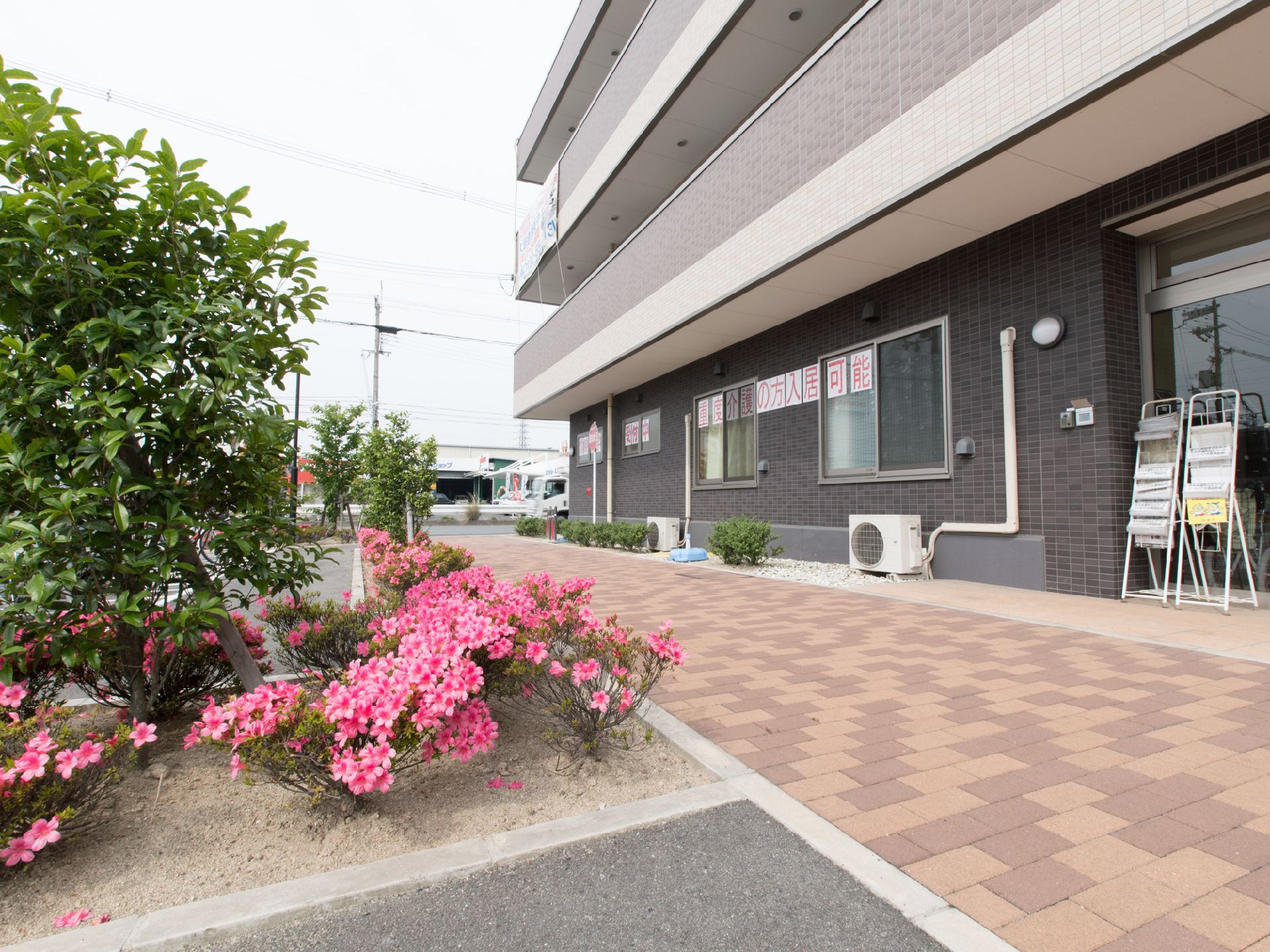 施設の前の歩道はレンガが敷いてあり、歩きやすく整備がされている。玄関前にはチラシを置くラックが置いてある。