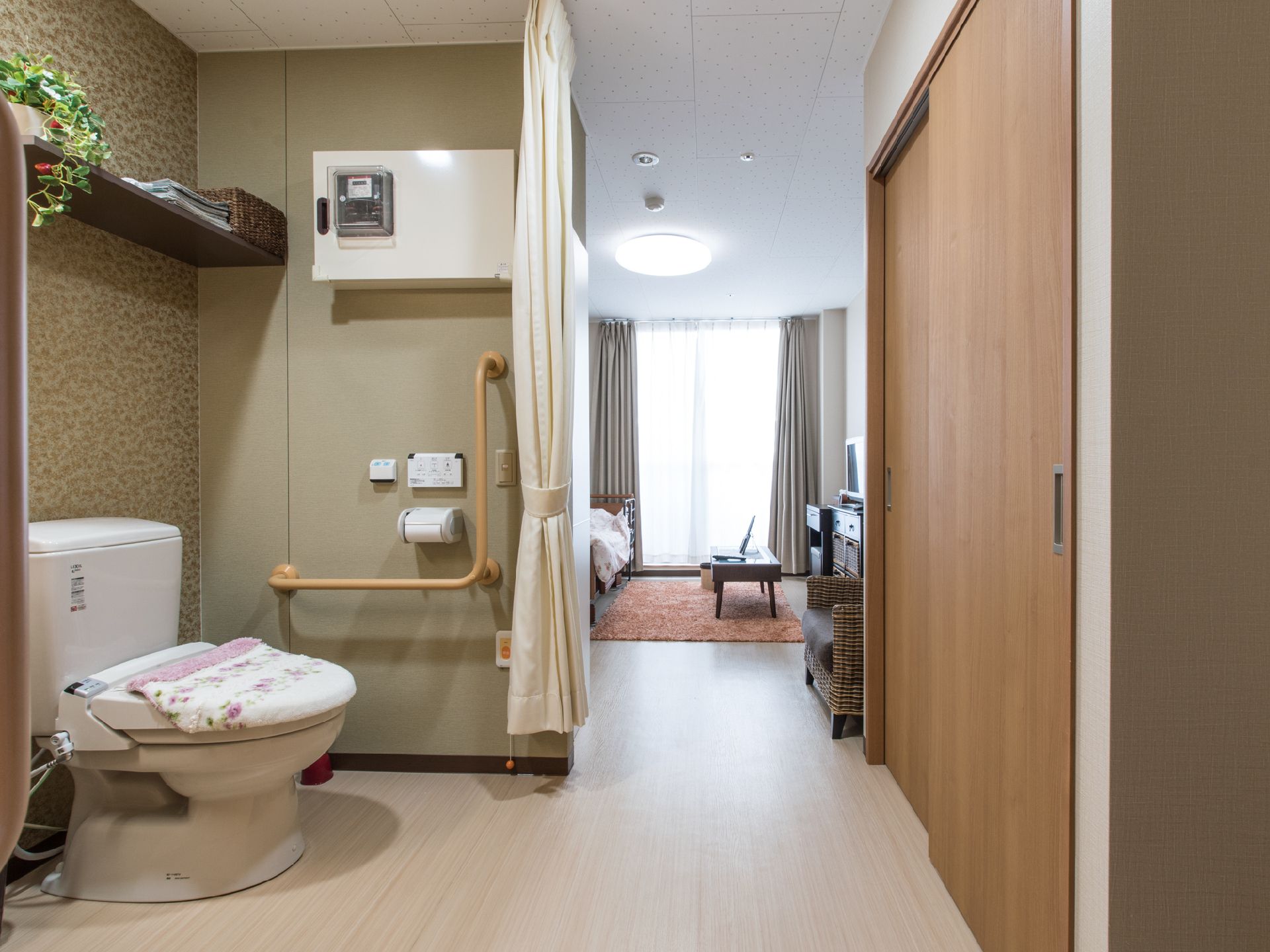 便座カバーがついた洋式トイレがある。手すりが左右についている。カーテンでしきることができ、バリアフリーで部屋につながっている。