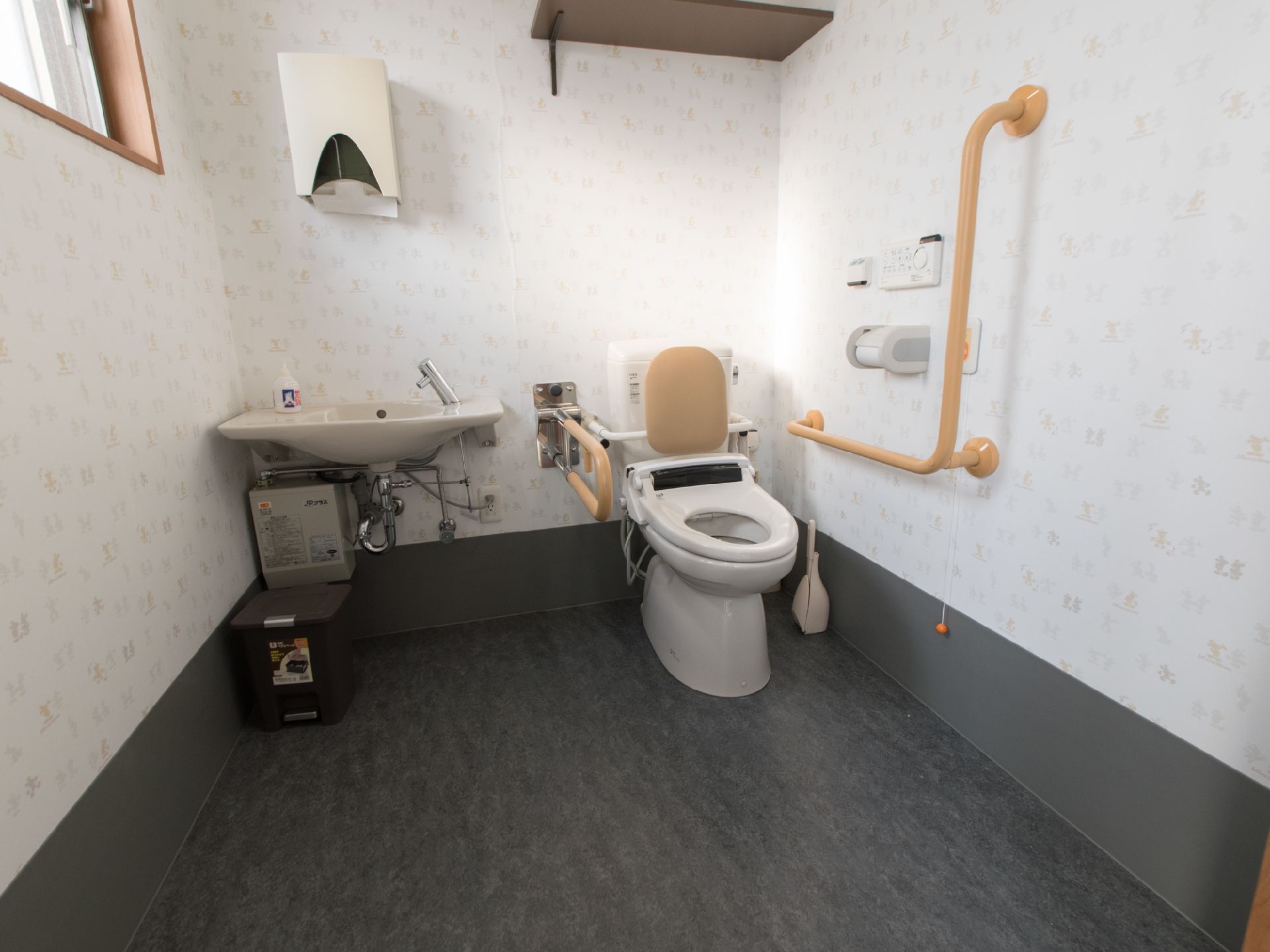 柄のついた壁紙のトイレで、両サイドに手すりがついていて、立ち居が楽になっている。気分が悪くなった時などに職員を呼べるブザーがついている。