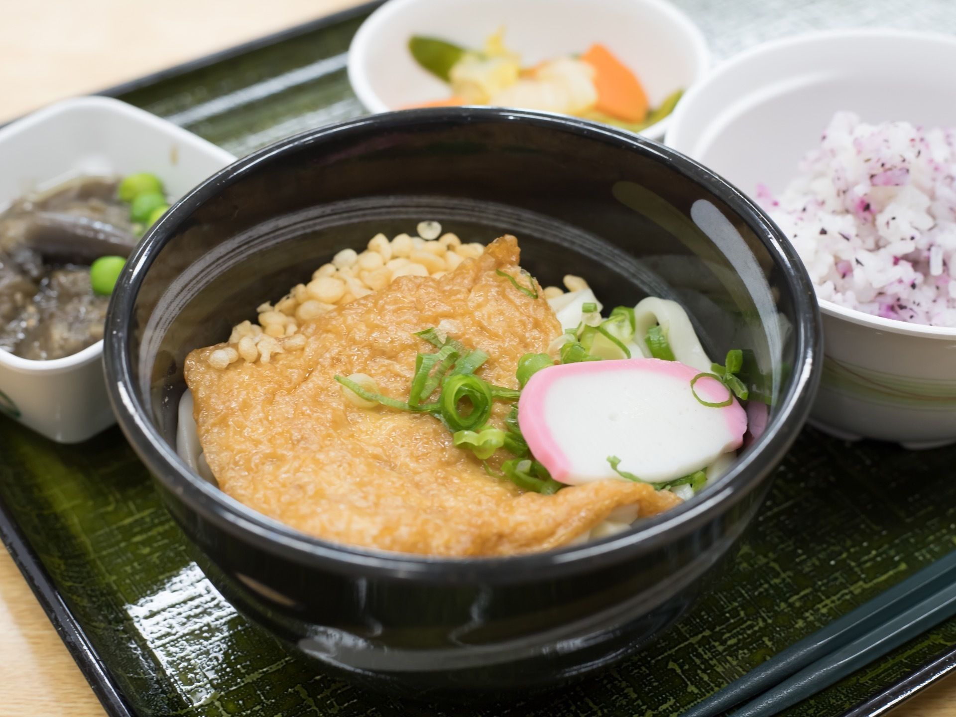 食事の一例。ゆかりごはんに漬物、なすの煮びたしが出される。メインにきつねうどんがあり、十分な食べごたえがある。