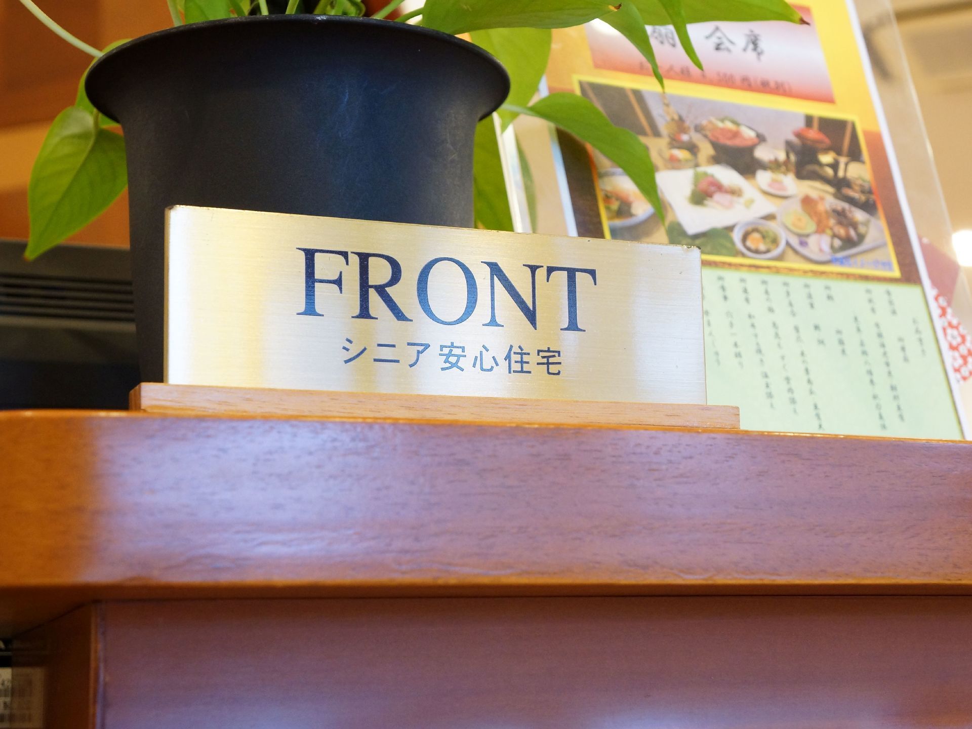 受付の様子である。金属製のプレートに受付を示す表示がある。レストランの案内なども置かれている場所である。