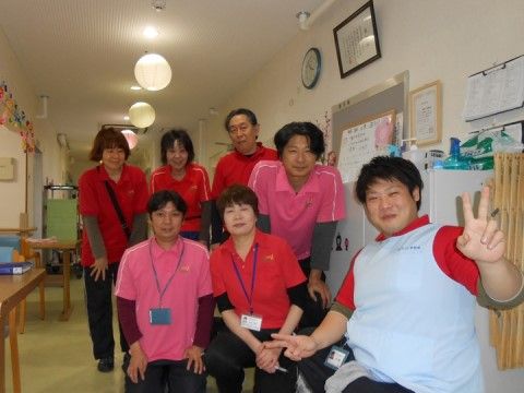 低い姿勢でこちらに笑いかけている７名のユニフォーム姿のスタッフ