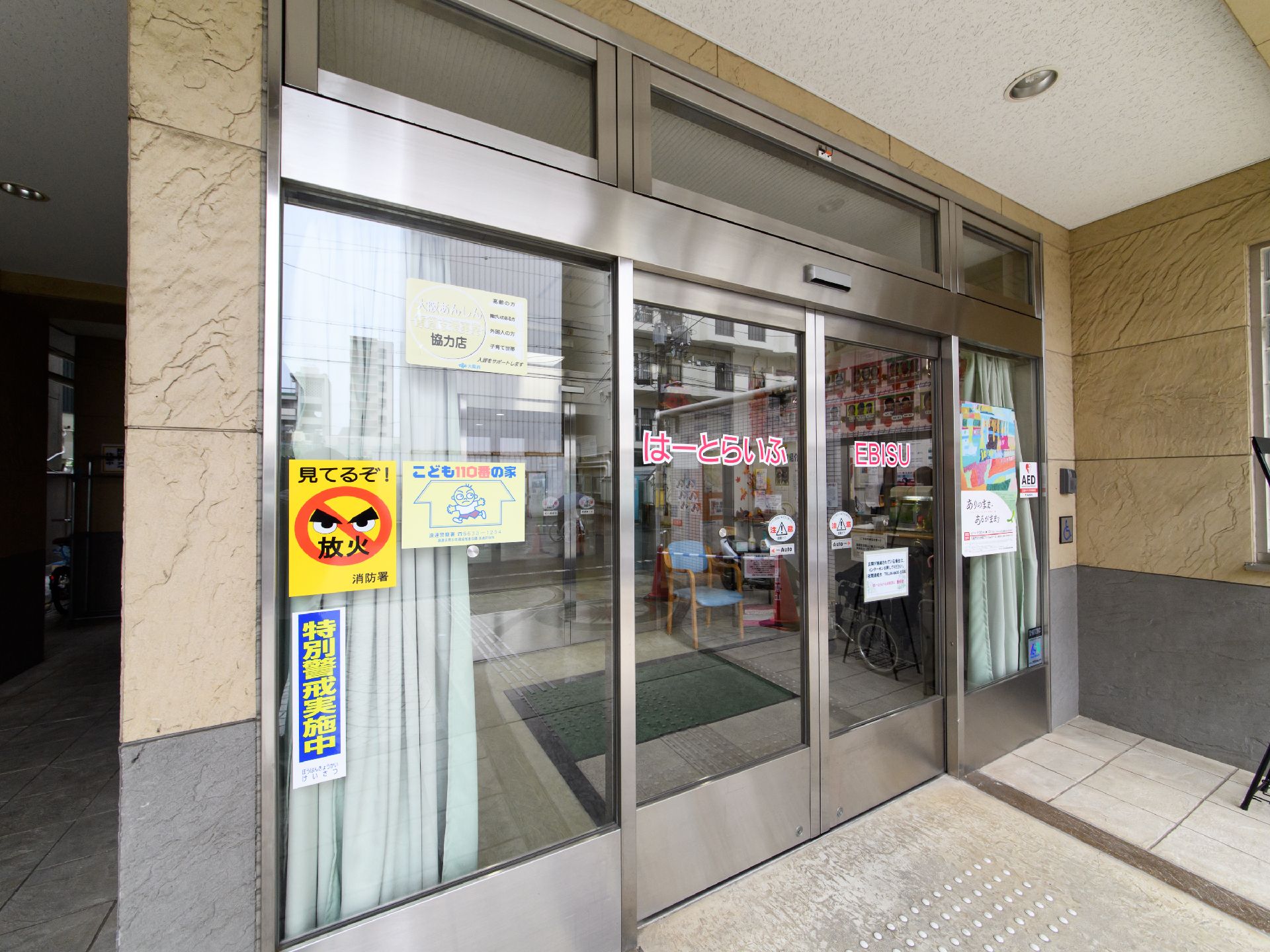 施設内に入るためには、自動ドアを2箇所通る必要がある。自動ドアには、施設名が表記され、ポスターが掲示されている。