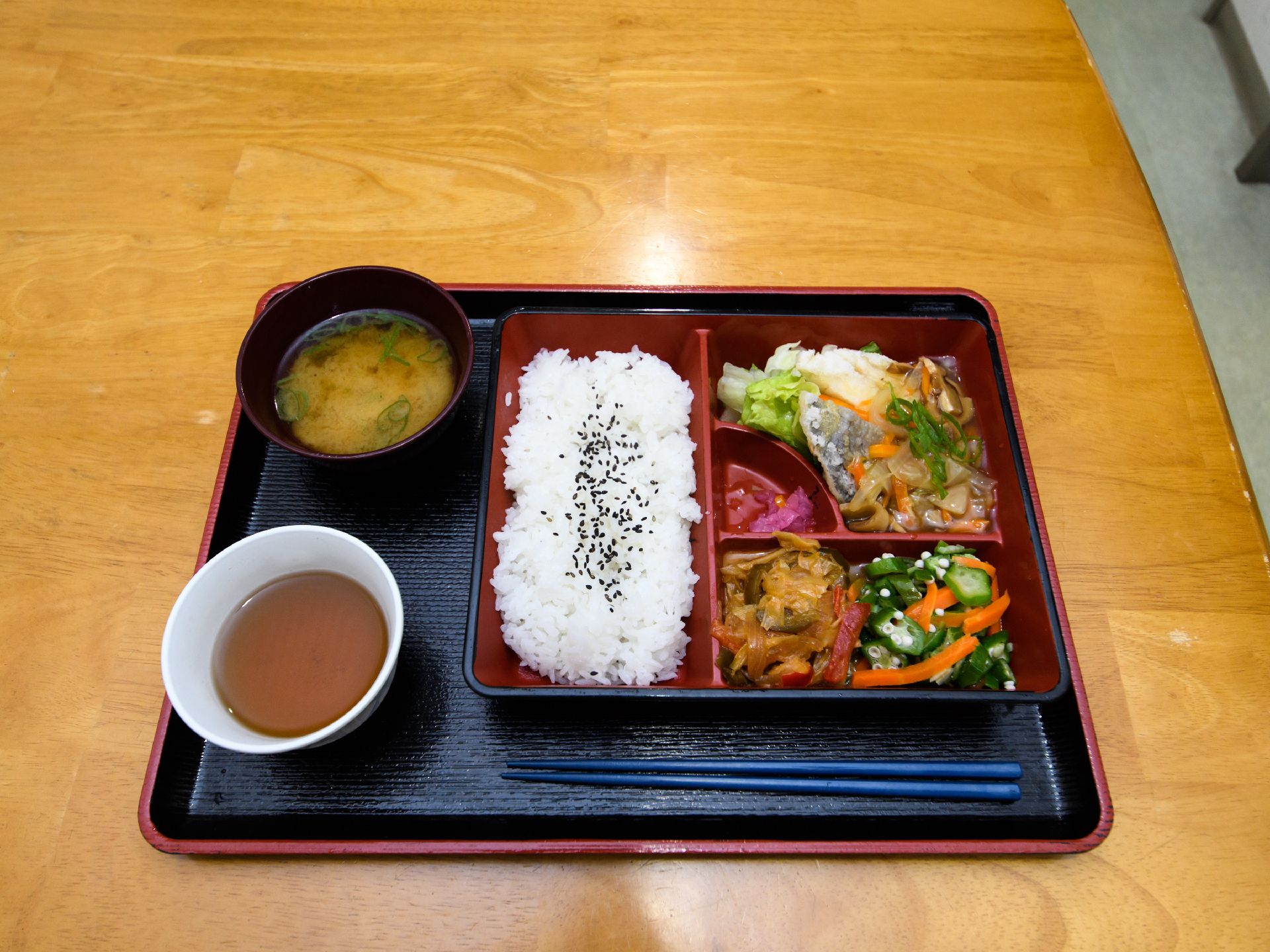 トレーの上に、料理と味噌汁、お茶、箸が載っている。白ご飯に魚料理、色とりどりの野菜が使用された料理がある。