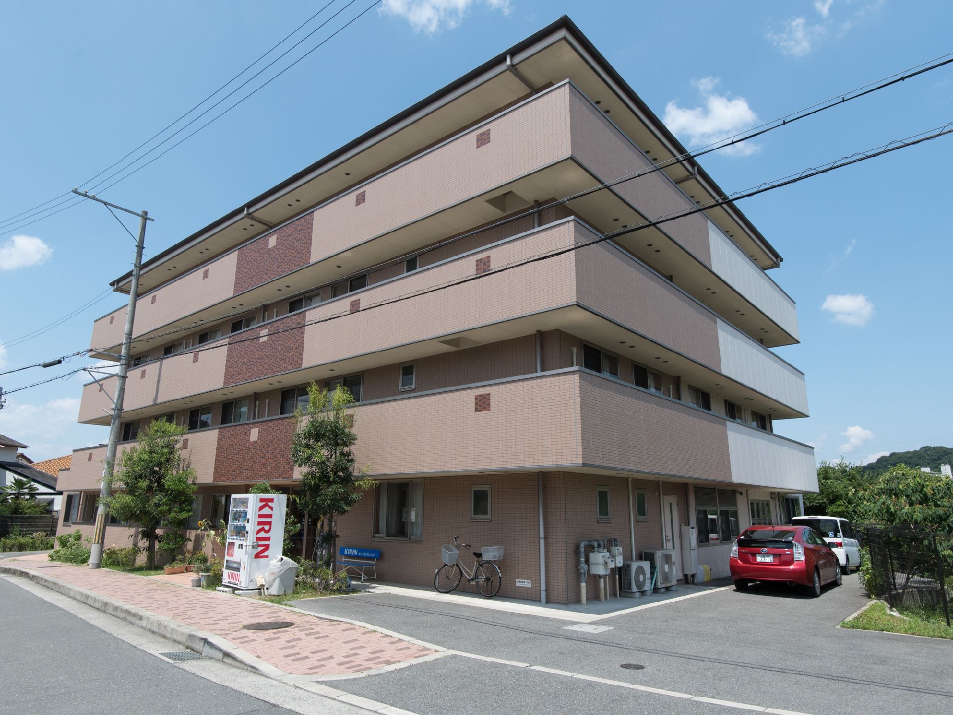 4階建ての大きな建物となっている。駐車場がある。自動販売機が置かれている。茶色で統一されてシックな雰囲気がある。