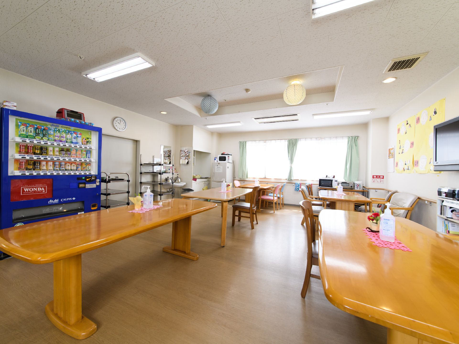 食堂には薄い緑色のカーテンが付いている。窓際には冷蔵庫が置かれている。茶色いテーブルが5つあり、周りには椅子が並べられている。
