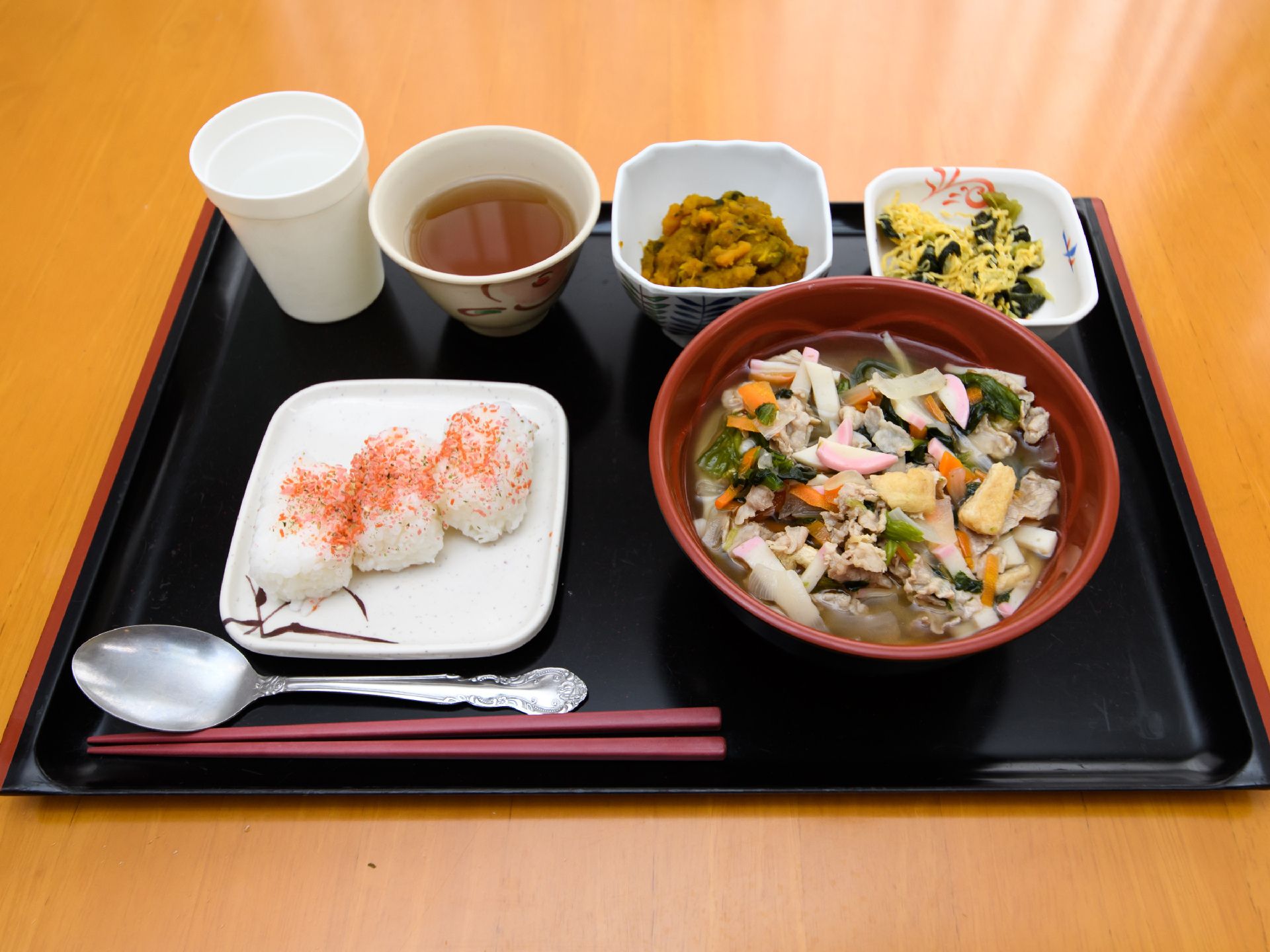 黒いお盆の上にはお箸と一緒にご飯や汁物、おかずが並べられている。ごはんは食べやすいように小さめのおにぎりにしている。