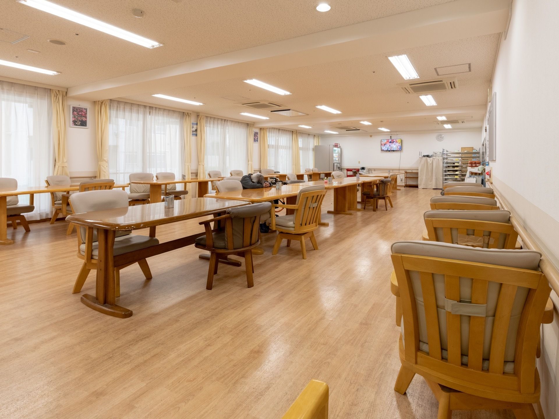 明るい茶色のテーブルが横長に配置されており、その周りには、座面がグレーの木製の椅子が並べられている。