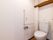 トイレには洋式タイプの便器を設置している。また室内には収納棚があり、壁には手すりが取り付けられている。