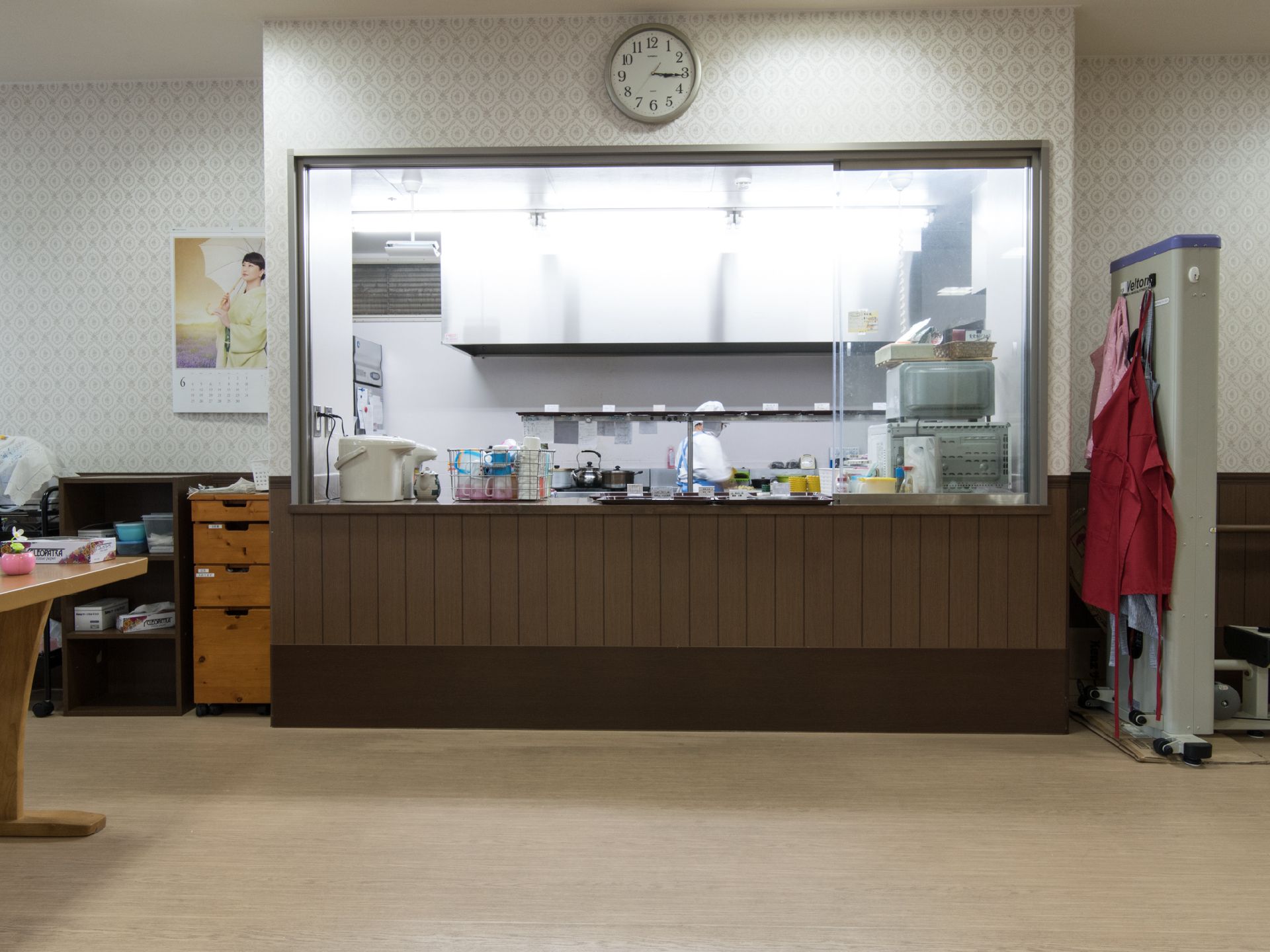 キッチンが見え、中で職員が調理をしている。髪の毛が入らぬように帽子をかぶり、エプロン、マスクを着用している。