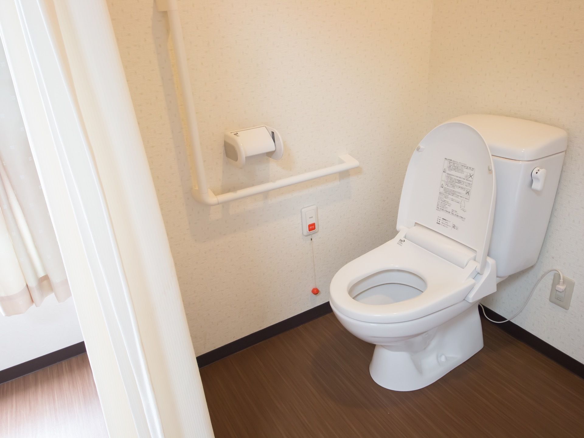 白色の洋式便座が設置された、清掃の行き届いたトイレである。壁に手すりが備え付けられており、安全に利用ができる。