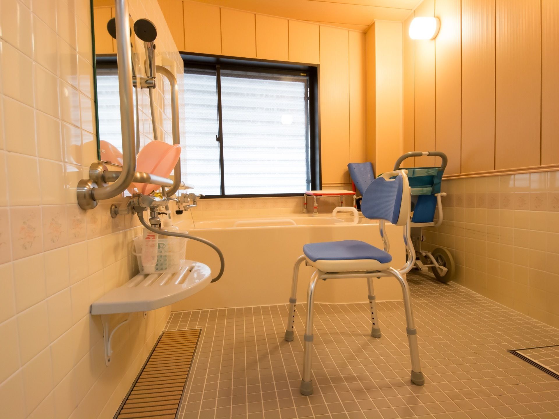 丸型の照明が浴室をあたたかく照らしている。ブルーのシャワーチェアなど、介護用の入浴グッズも完備している。