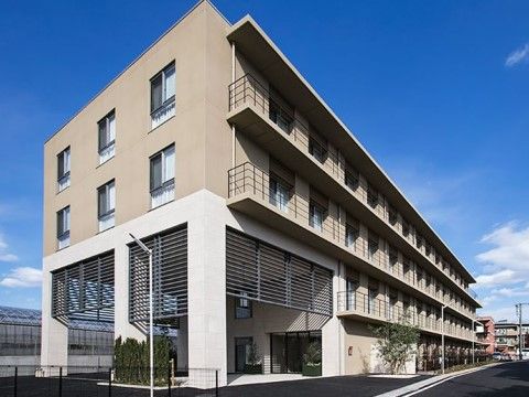 4階建ての建物は横に長く、2階から4階部分にはベランダが付いている。公道に面しており、所々に植え込みが配置されている。