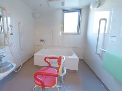 白を基調とした清潔感が漂う浴室である。手すりやシャワー、浴室用の介護用の椅子、非常呼び出しブザーの完備で快適な入浴ができる。