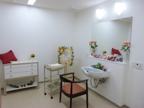 白を基調とした清潔な印象の室内に、理容用のシンクや鏡を備えている。道具の入ったカートも置かれている。