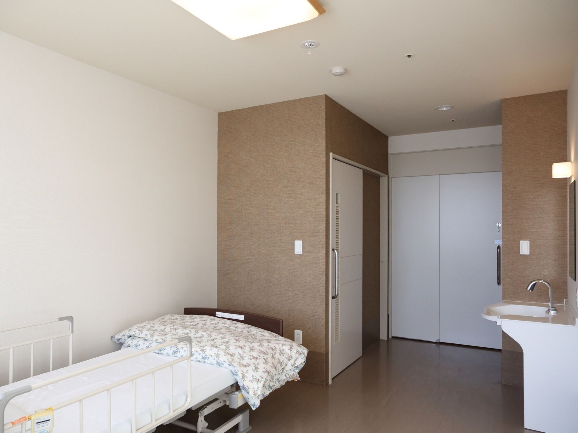 白い壁に茶系の床がスッキリとしたデザインの居室である。扉の幅は広く、入り口付近にトイレや洗面スペースが設けられている。