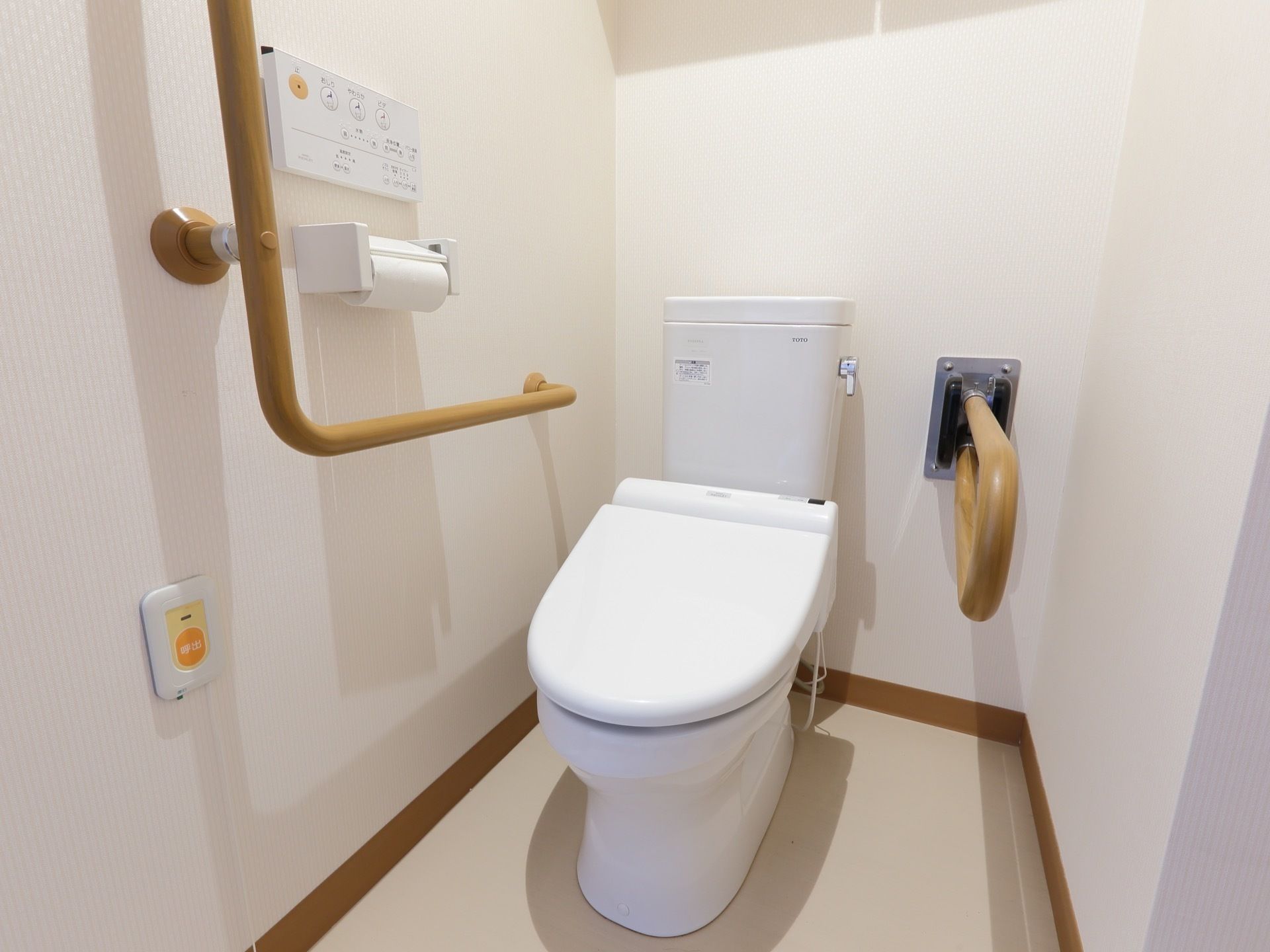 白い壁とベージュの床が明るい雰囲気のトイレには手すり、緊急の場合にも安心の通報装置が設置されている。