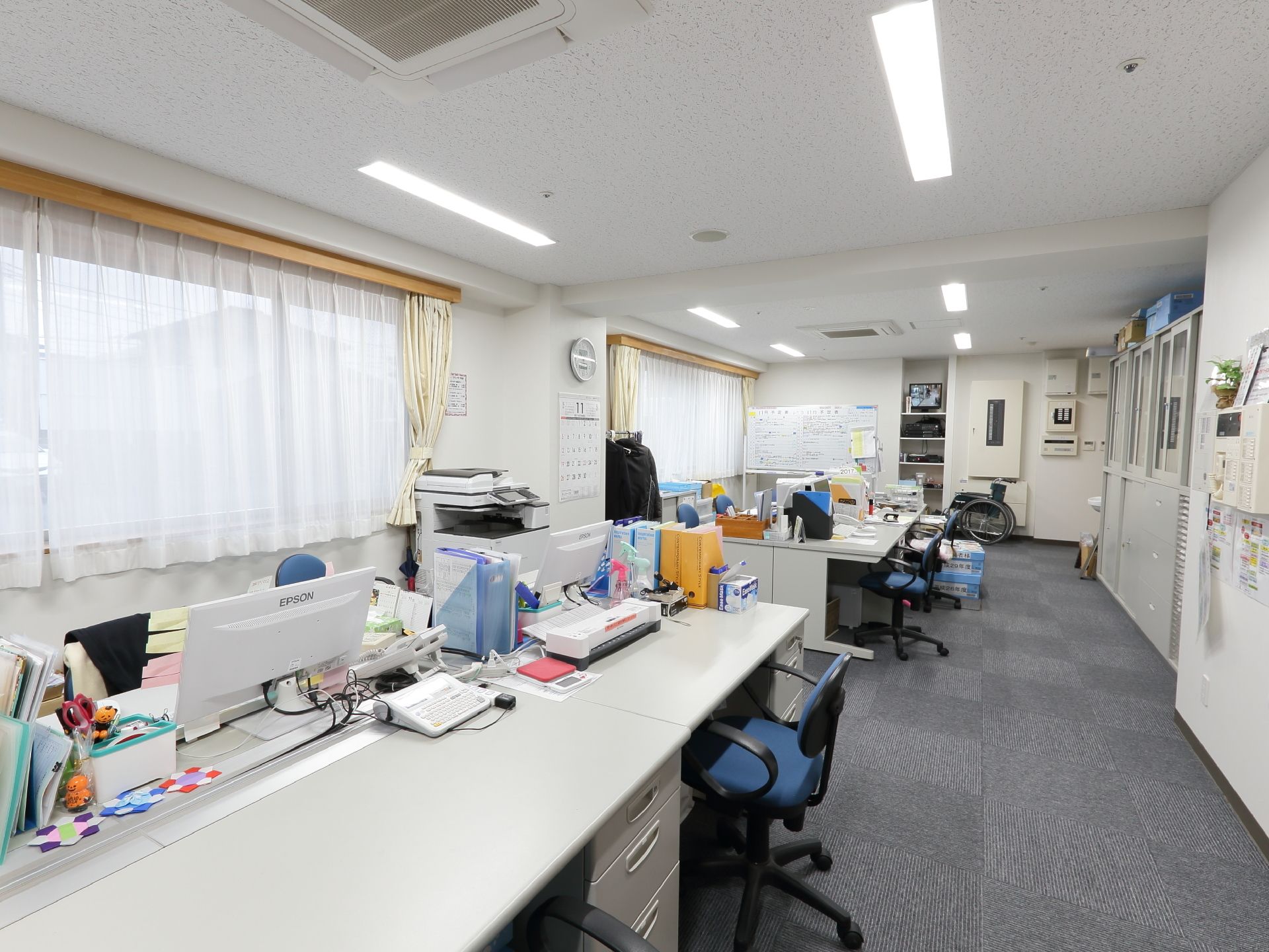 大きな窓に面した広々としたスタッフルームには机や椅子、コピー機、キャビネットがきちんと並べられている。