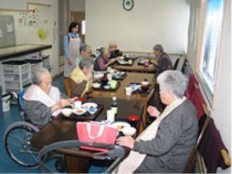 エプロン姿の女性スタッフが見守る中ダイニングでの入居者様皆さまの食事風景