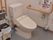 洋式トイレで、呼び出しブザーが手すり下設けてあり、座りながら利用できるよう、ひもが長くなっている。不要タオル回収のボックスがある。