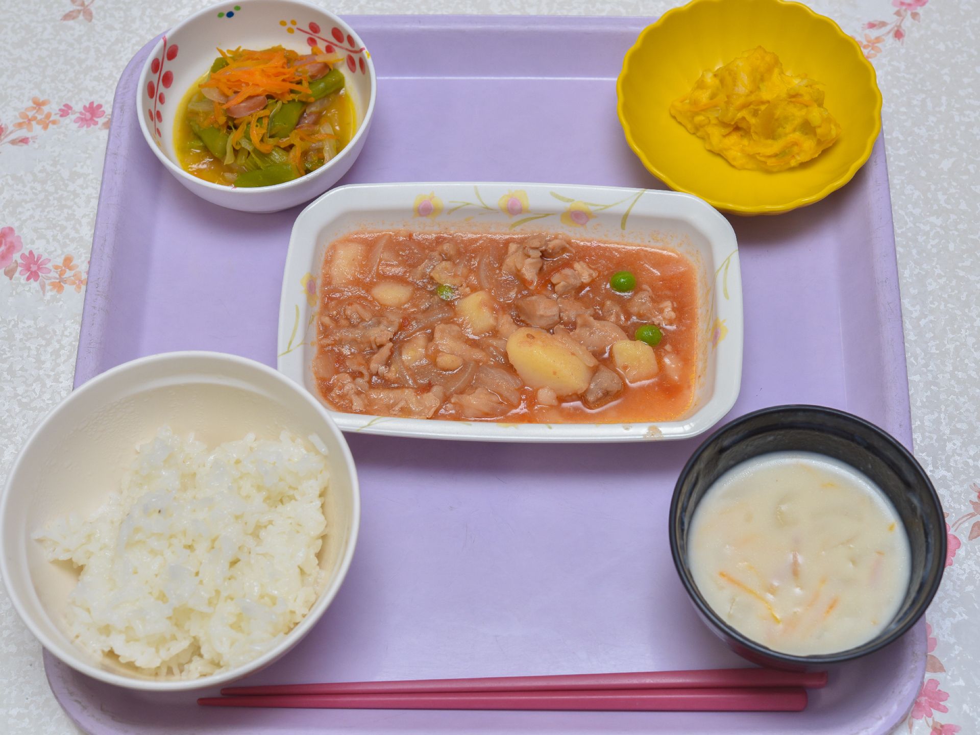 淡いパープルのトレーの上に1人分の食事がセットされている。一番手前に赤い箸が置かれ、ご飯と汁物、おかずが3品並んでいる。