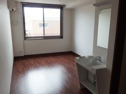 部屋の奥の壁の中央にある大きめの窓から光が差し込む居室。部屋の中には足下にスペースがあるタイプの洗面台が設置されている。