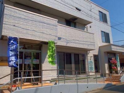 落ち着いたブラウン系の外壁の３階建ての建物。建物正面の２階３階にはバルコニーがついていて、入口のひさし代わりになっている。