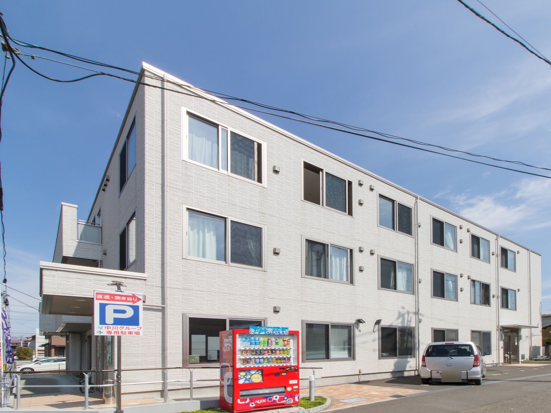 ３階建ての建物の手前には、数台停められる駐車スペースがある。一角には飲み物の自動販売機が設置されている。