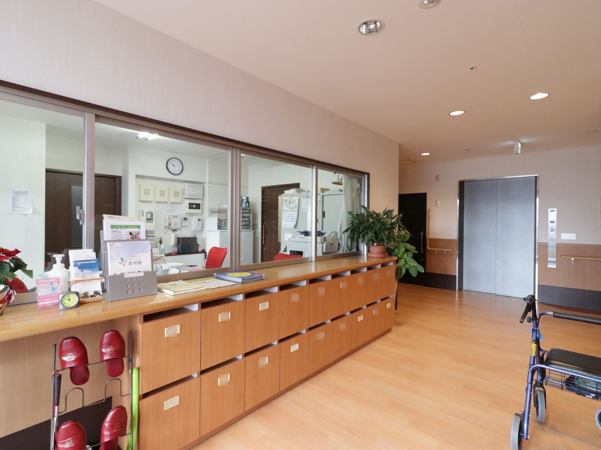 玄関には入居者様ごとに扉が付いた靴箱が設置されている。大きなガラス窓で仕切られたスタッフルームがある。