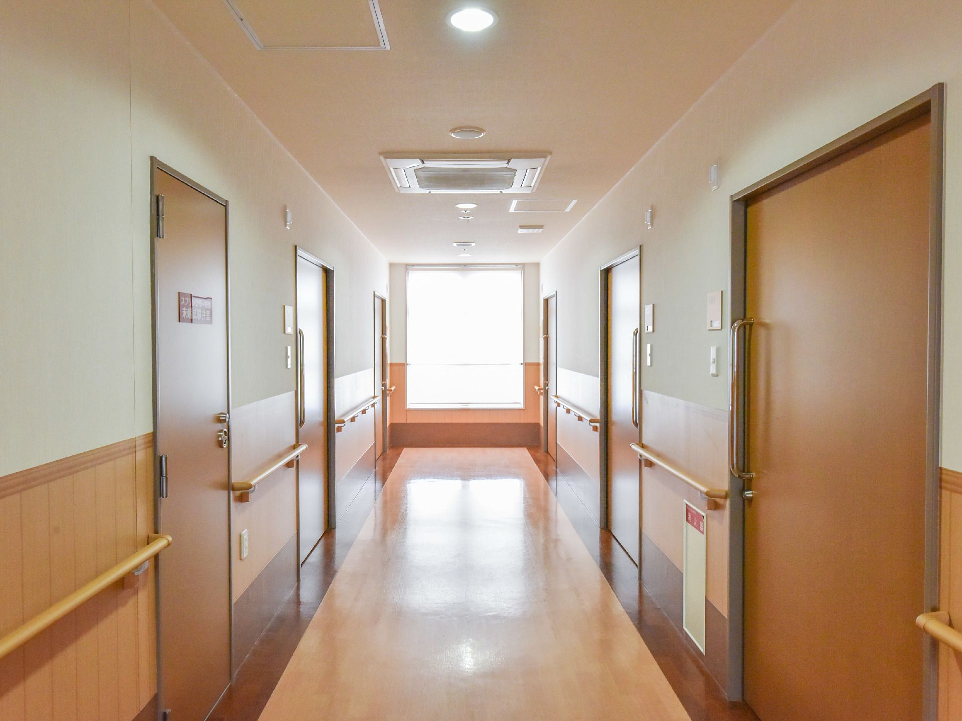 廊下の奥には窓があり、とても明るい。壁には手すりが取り付けられている。車椅子でも余裕がある広さがある。