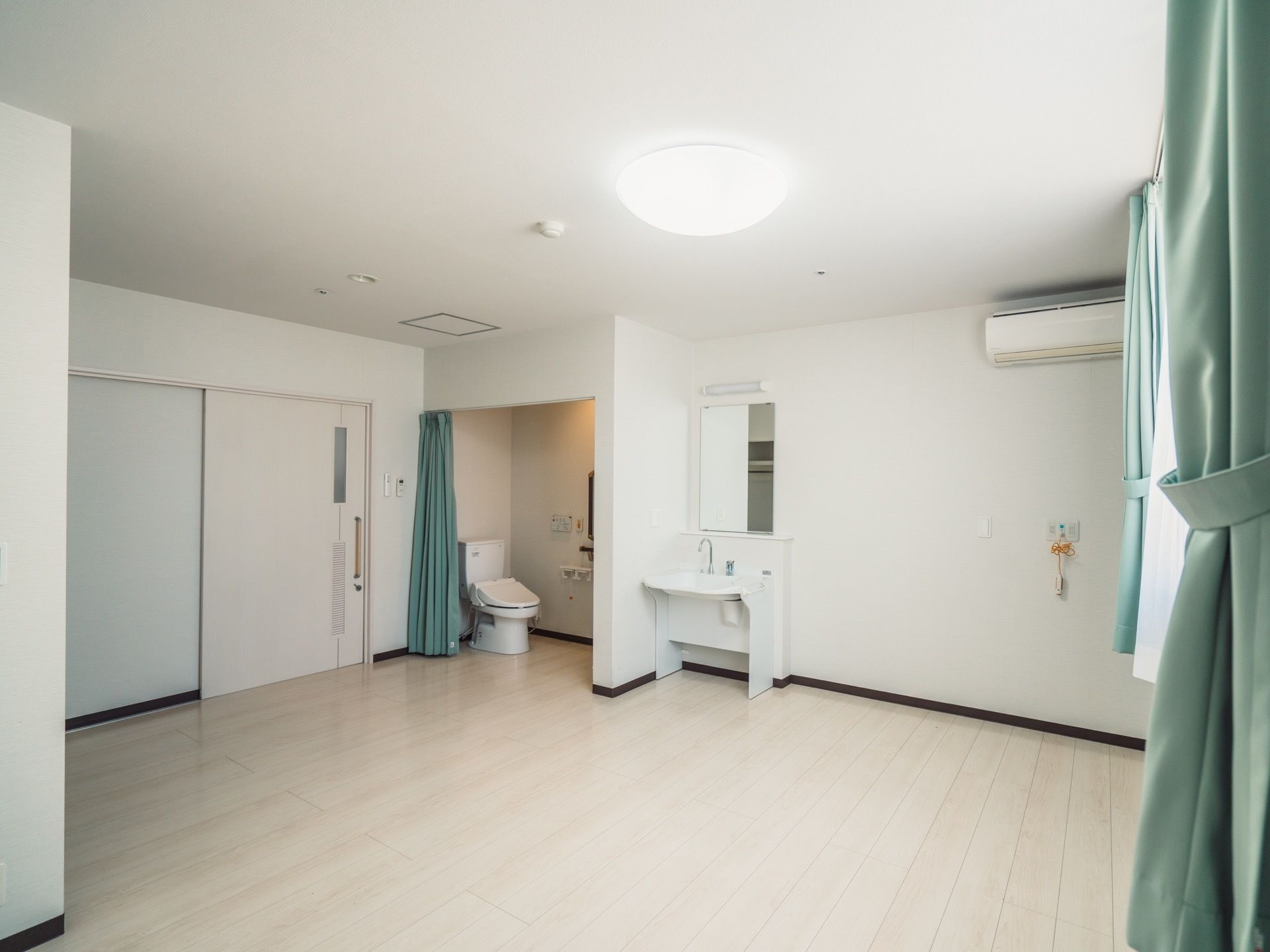 清潔感のある白色を基調とした居室である。トイレや洗面台、エアコンが設置されている。トイレはカーテンで仕切られており、出入りが簡単である。